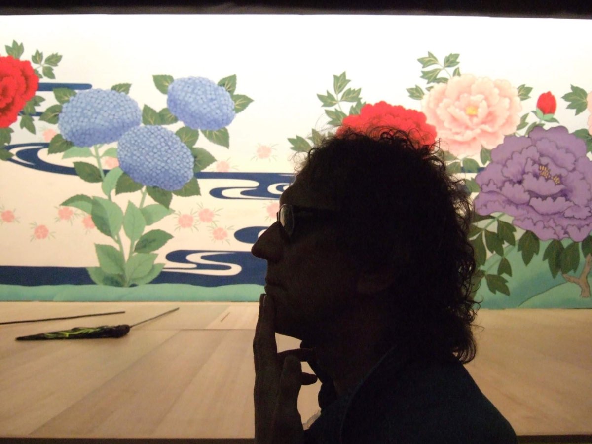 Mick Rock in profile, hand to his mouth, before a painted floral backdrop at the Kabukiza theatre, Tokyo.