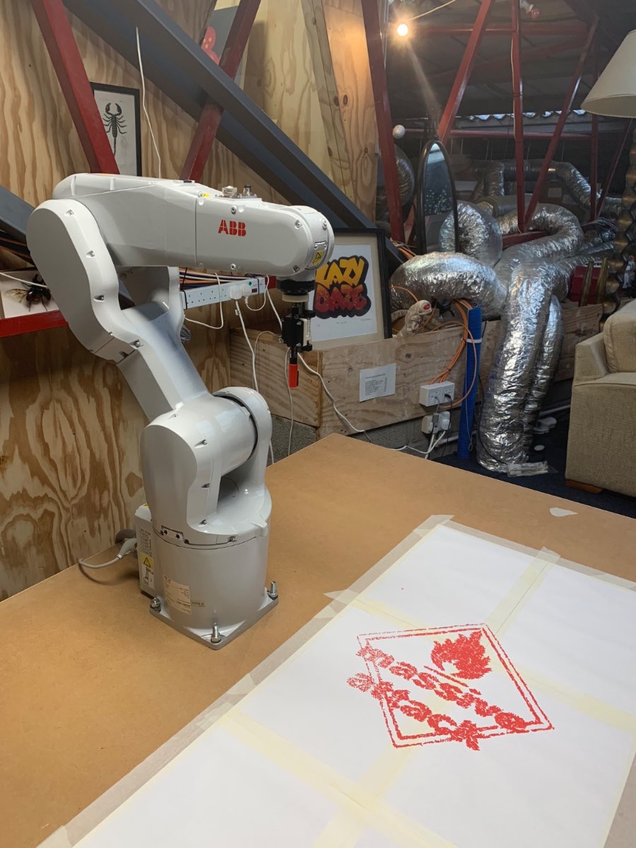 An ABB robot arm stamping the Massive Attack mark in red onto paper.