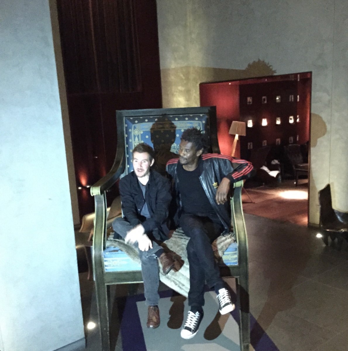 Andrew Melchior seated with Robert Del Naja in an oversized chair.