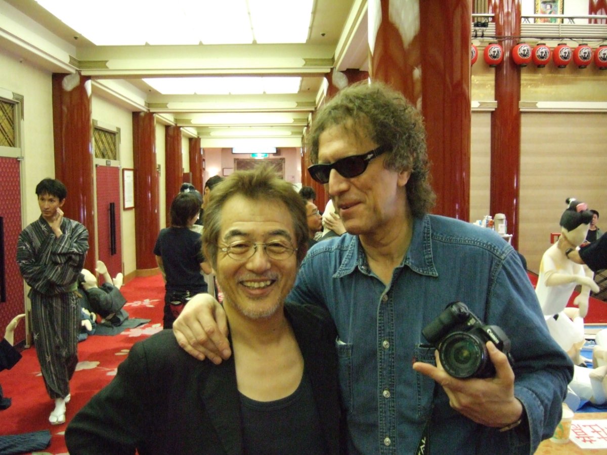 Andrew Melchior with Mick Rock, who is holding a camera, in an ornate room.