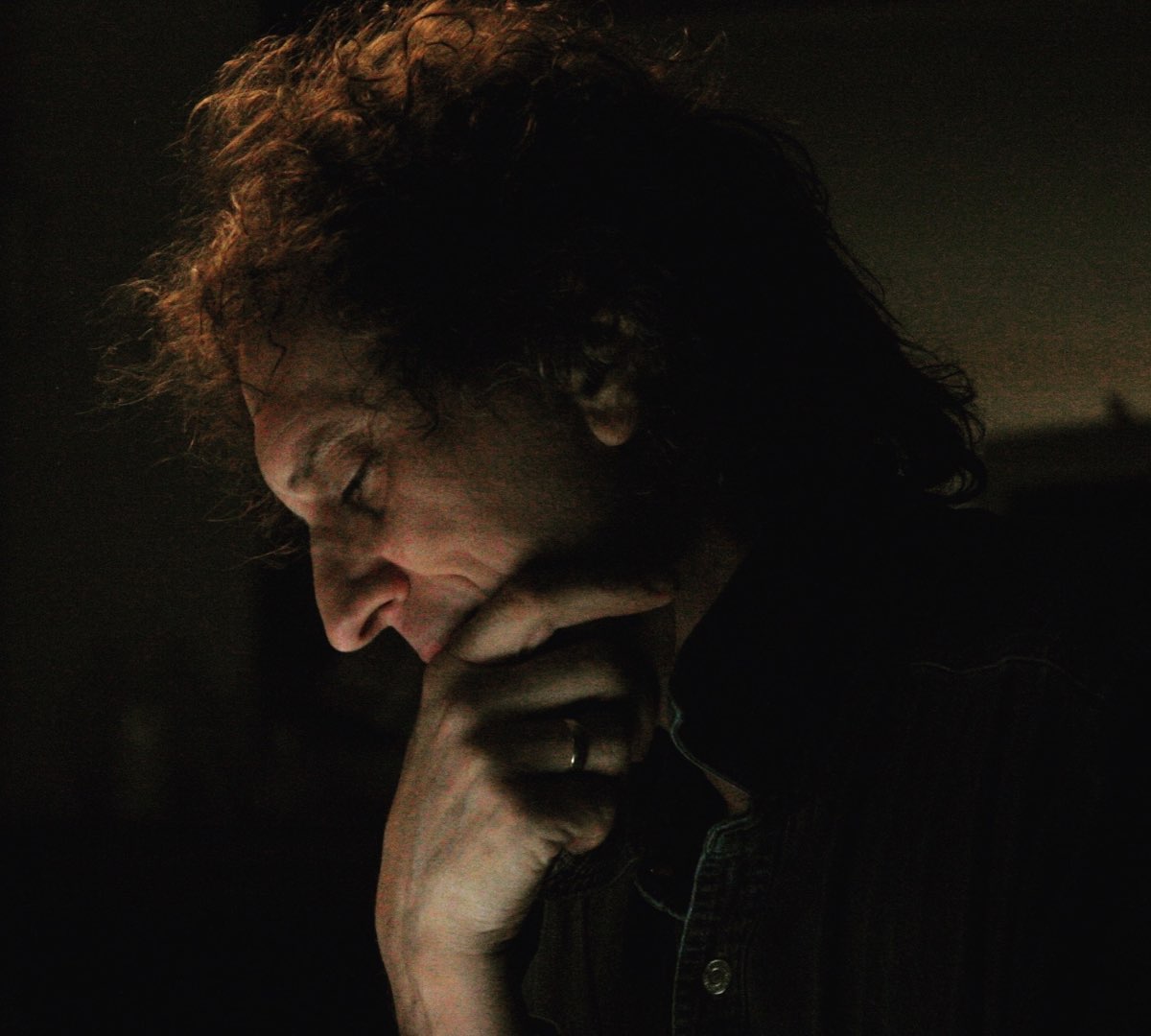 Portrait of the photographer Mick Rock in low light, hand to his face.