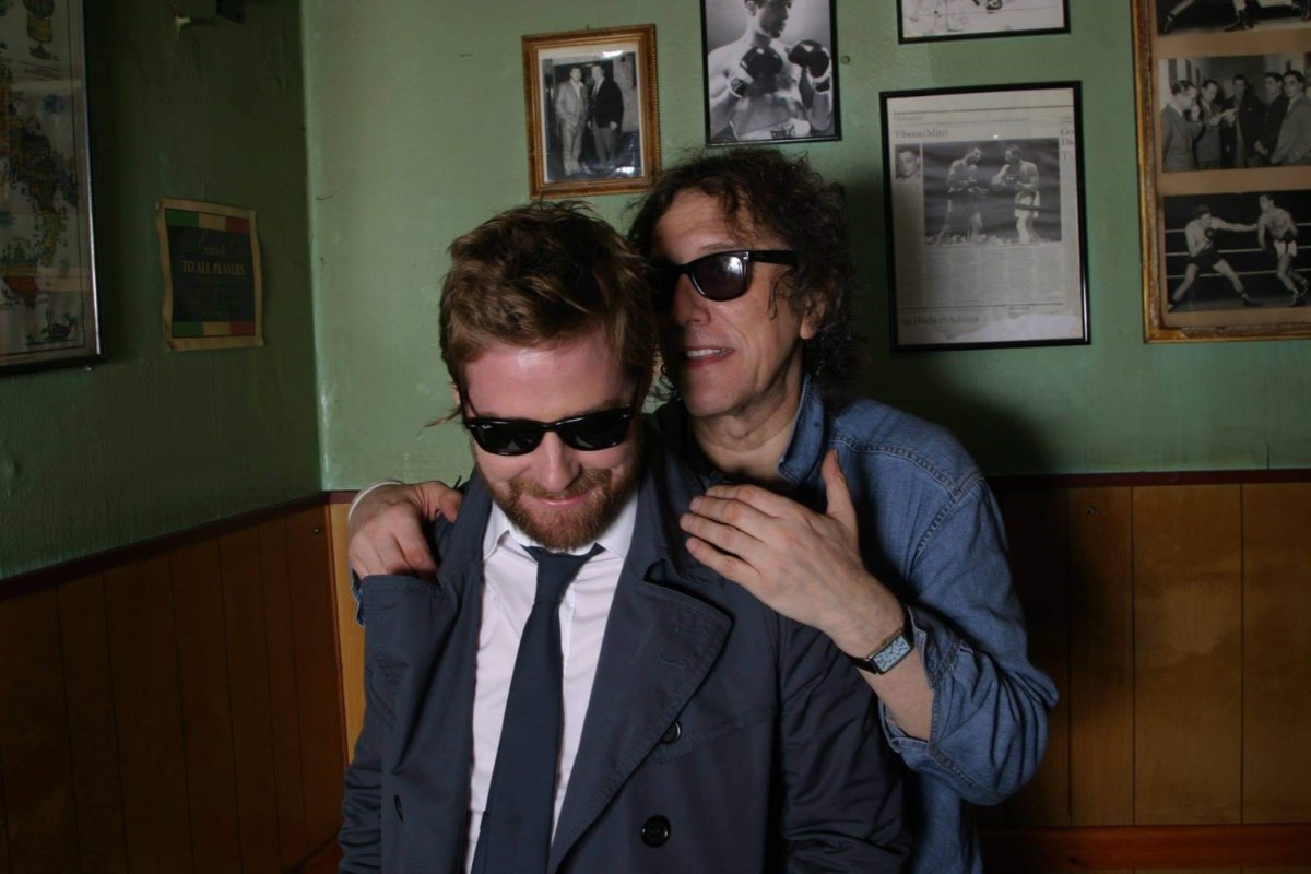 Andrew Melchior and a subject in sunglasses beneath framed boxing photographs.
