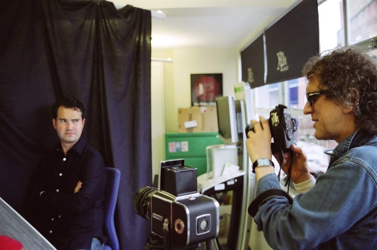 Mick Rock working with a medium-format camera against a black studio backdrop.