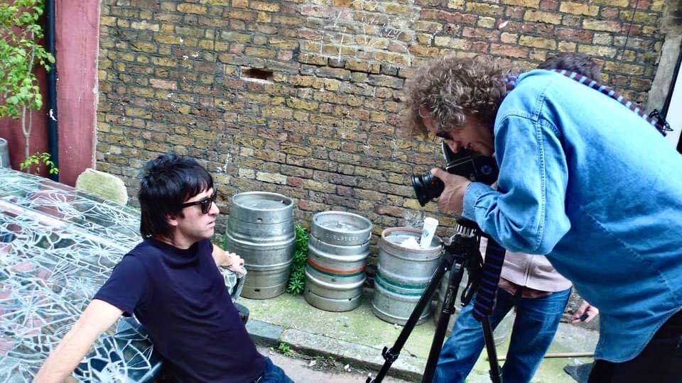 Mick Rock photographing a subject in an alley among beer kegs.