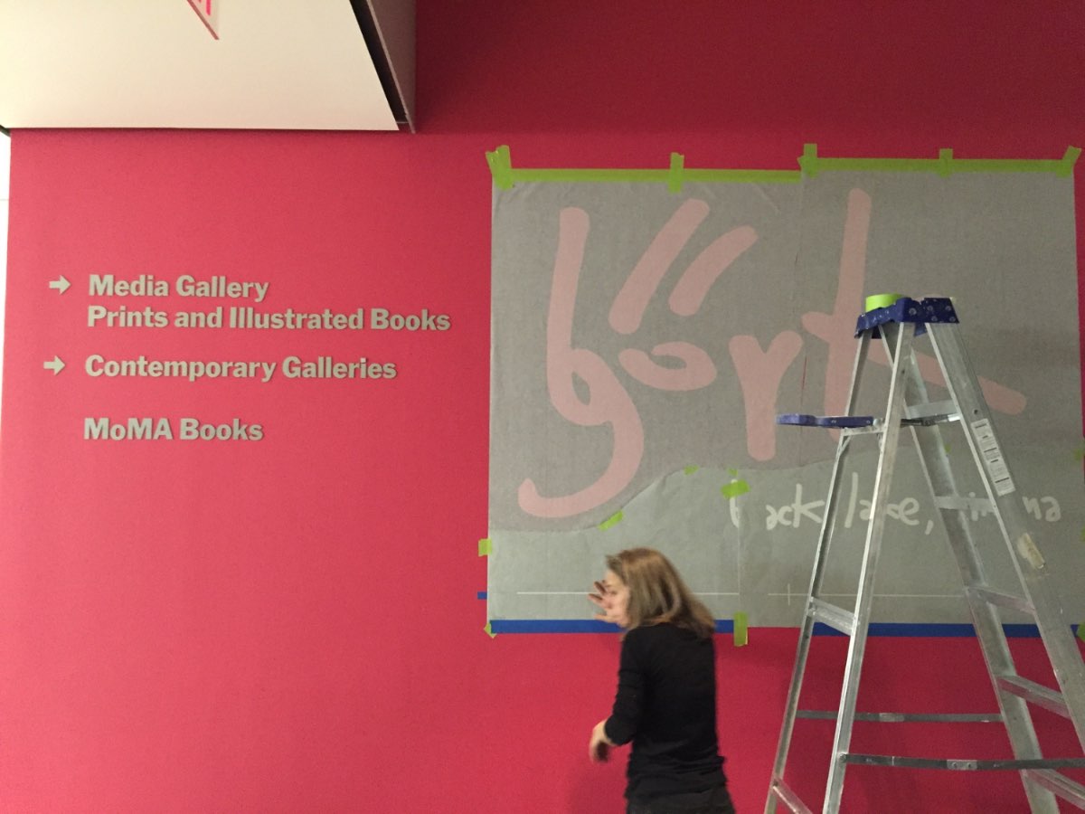 A magenta gallery wall being installed with Björk's handwritten name and the Songlines exhibition text at MoMA.